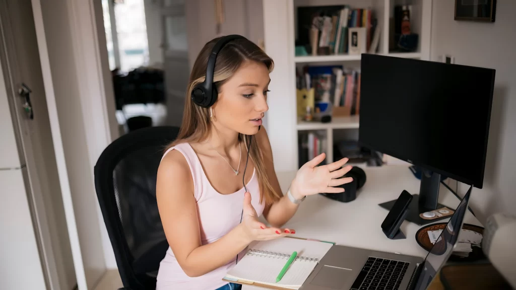 Young-woman-working-remotely-wearing-headphones-and-engaging-in-a-video-call-at-her-home-office